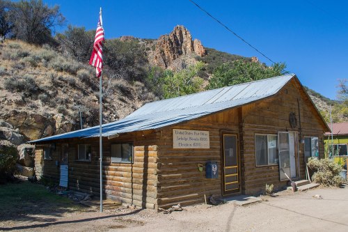 A rustic wooden building with a flag, set against rocky hills under a clear blue sky.