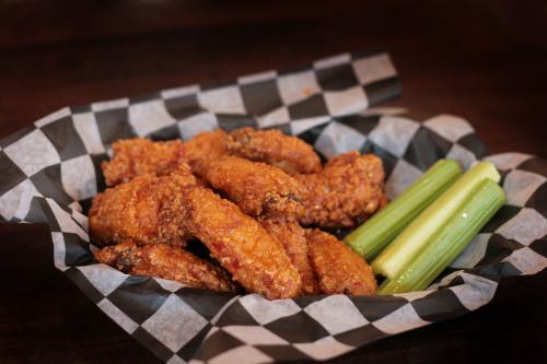 A basket of crispy fried chicken wings served with celery sticks on a checkered paper liner.