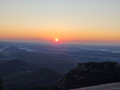 A serene sunrise over rolling hills, with soft colors illuminating the sky and mist rising from the valleys below.