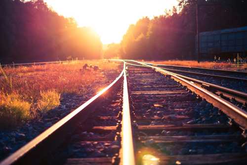 Sunset over a railway track, with golden light illuminating the rails and surrounding grass.