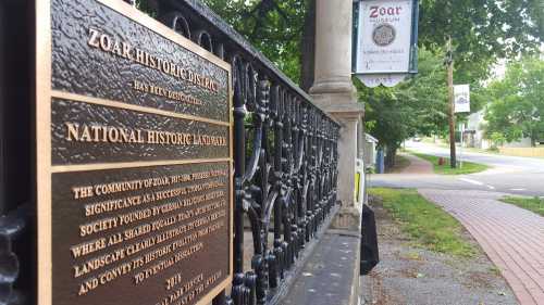 Plaque detailing the Zoar Historic District, with a sign for the Zoar Museum and a view of the street.