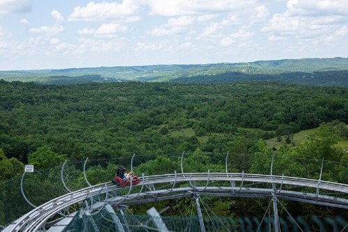 A scenic view of lush green hills with a roller coaster track winding through the landscape under a blue sky.
