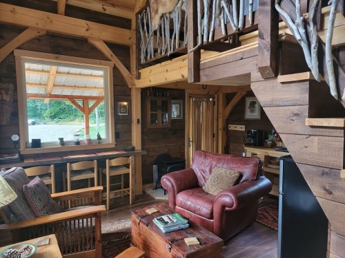 Cozy wooden cabin interior with a red leather sofa, rustic decor, and a lofted sleeping area. Natural light from windows.