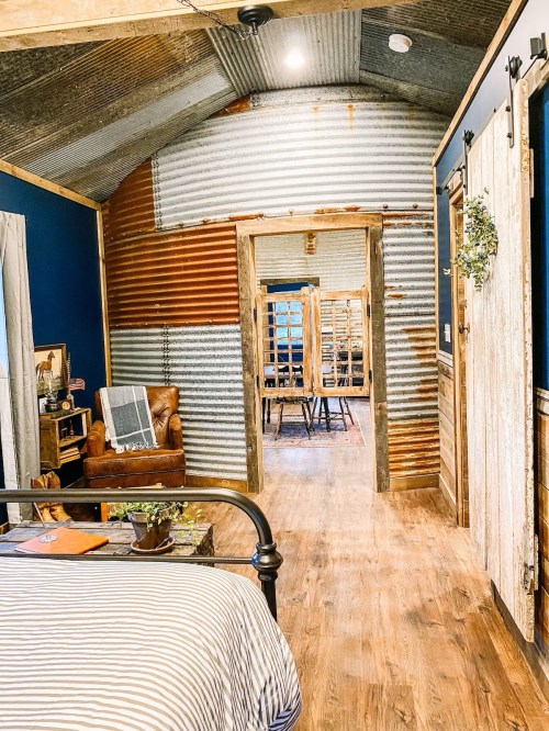 Cozy room with corrugated metal walls, wooden accents, and a view into a rustic dining area.