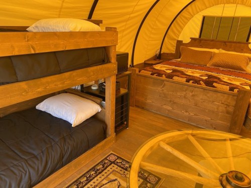 Interior of a cozy tent featuring a bunk bed and a queen-sized bed, with wooden furniture and a decorative rug.