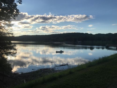 A serene lake at sunset, with clouds reflecting on the water and a small boat in the distance.
