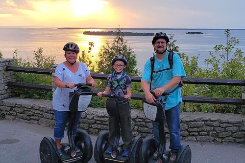 A family of three on Segways at sunset, with a scenic view of water and trees in the background.