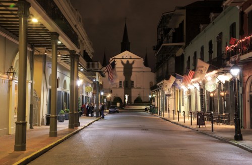 Quiet street at night with historic buildings, a church in the background, and festive decorations along the sidewalks.