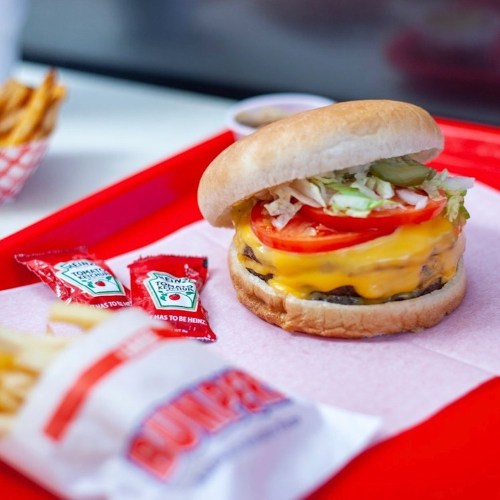 A cheeseburger with lettuce, tomato, and pickles on a tray, accompanied by fries and ketchup packets.