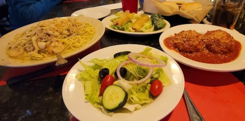 A table setting with pasta, salad, spring rolls, and meatballs in marinara sauce, all on red placemats.