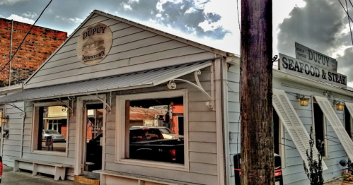 Exterior of Dupuy Seafood & Steak restaurant, featuring a light blue building with large windows and a sign above.