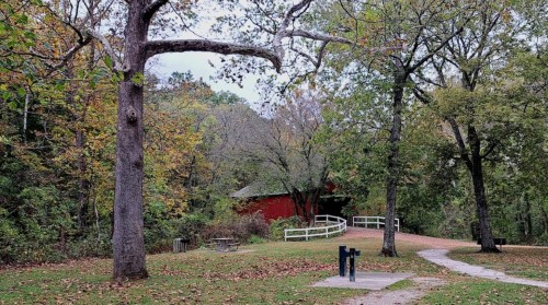 A scenic path leads to a red barn surrounded by trees and autumn foliage in a peaceful outdoor setting.