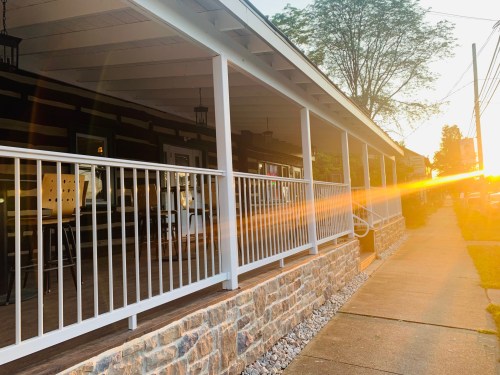A sunlit porch with white railings and stone walls, casting a warm glow in the evening light.