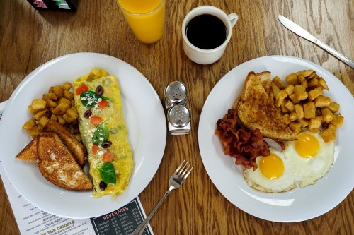 A breakfast spread featuring an omelet, bacon, eggs, toast, and potatoes, with coffee and orange juice on the side.