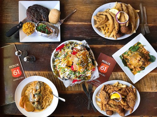 A spread of various dishes including steak, seafood, salads, and fried foods on a wooden table with a menu.