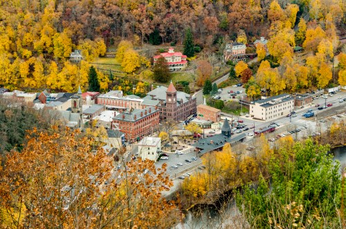 Aerial view of a small town surrounded by autumn foliage, featuring historic buildings and a winding road.