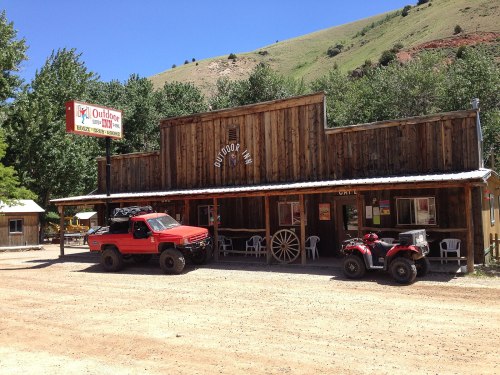 A rustic wooden building with a sign reading "Outdoor Inn," featuring a red truck and an ATV parked outside.
