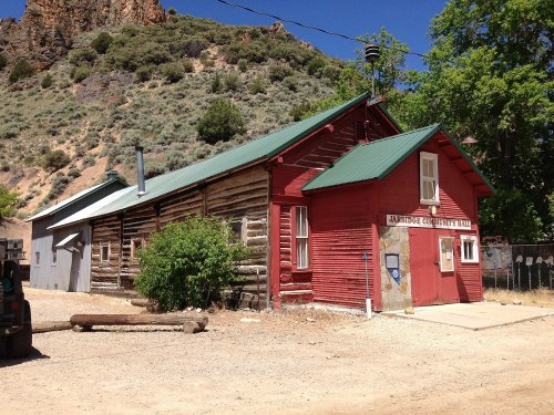 A rustic red building with a green roof, surrounded by trees and mountains, labeled "Arbuckle County Fair."