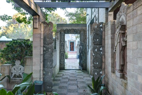 A stone pathway leads through intricately carved archways, surrounded by greenery and sculptures.
