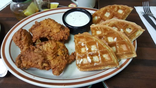 A plate with two pieces of fried chicken, three waffles, and a small cup of dipping sauce.