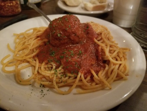 A plate of spaghetti topped with marinara sauce and a large meatball, garnished with parsley.