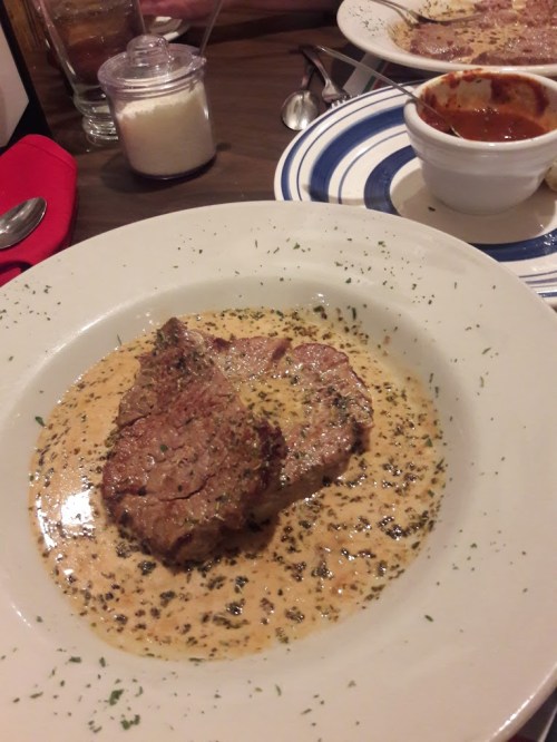 A plate of sliced beef in a creamy sauce, garnished with herbs, served with a side of chili in a small bowl.