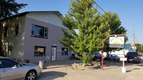 A two-story building with a sign for "West End Pub" and a large tree in front, surrounded by parked cars.