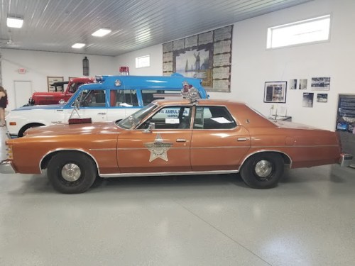 A vintage brown police car with a star emblem, displayed in a museum alongside other classic vehicles.