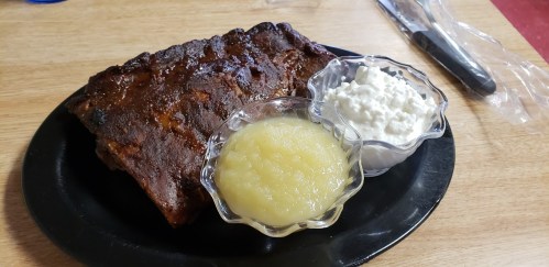 A plate with a piece of barbecued meat, served with applesauce and cottage cheese in small bowls.