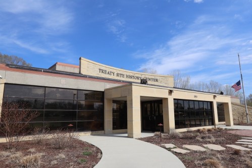 Exterior view of the Treaty Site History Center, featuring large windows and a pathway, under a blue sky.