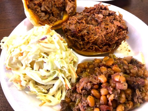 A plate with pulled pork on a bun, coleslaw, and baked beans.