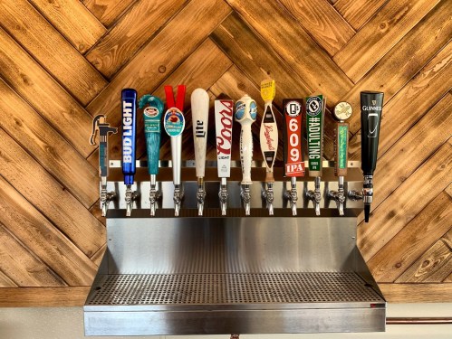 A row of beer taps featuring various brands against a wooden backdrop.