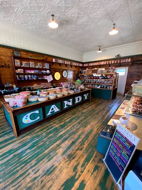 A colorful candy shop interior with wooden floors, shelves filled with jars, and a large "CANDY" sign.