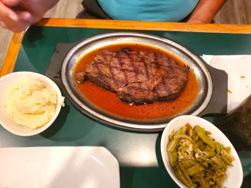 A sizzling steak on a plate, accompanied by mashed potatoes and green beans on the side.