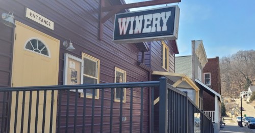 A winery building with a sign, featuring a yellow door and a railing, set in a small town.