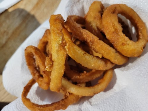 A pile of golden-brown, crispy onion rings on a paper towel.