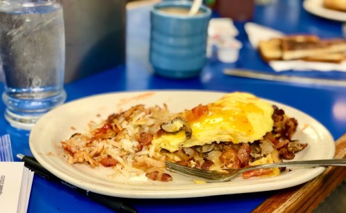 A plate of breakfast featuring an omelet, hash browns, and a fork, set on a blue table with a glass of water.