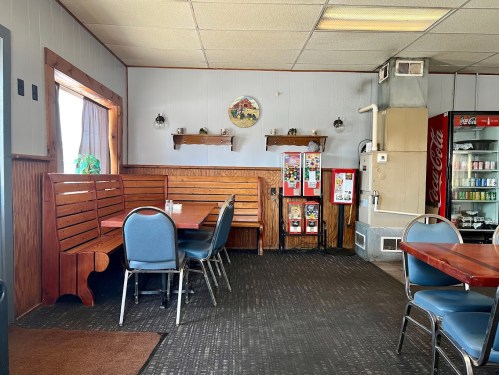 Cozy diner interior with wooden booths, tables, and a soda machine, featuring a rustic decor and warm lighting.