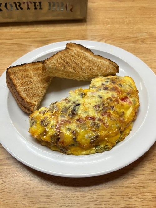 A plate with a cheesy omelet filled with vegetables and meat, accompanied by two slices of toasted bread.