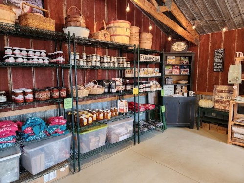 A cozy farm store interior with shelves of jars, baskets, and local products, illuminated by warm string lights.