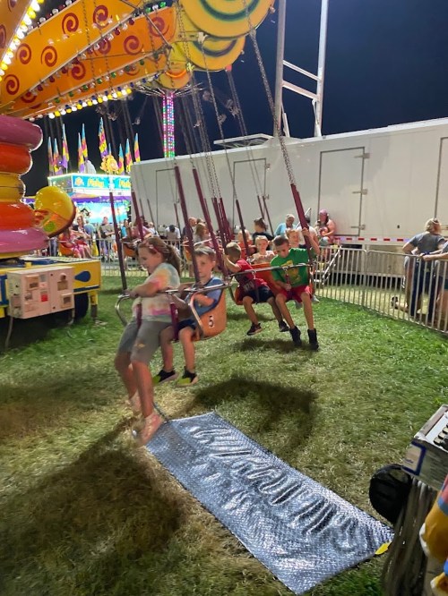 Children enjoying a swing ride at night, surrounded by colorful lights and a festive atmosphere.