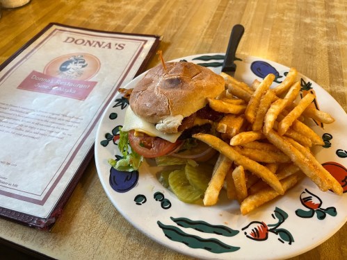 A burger with lettuce, tomato, and cheese on a plate, accompanied by a side of crispy French fries and a menu.