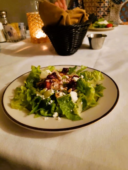 A fresh salad with greens, beets, and feta cheese on a white plate, set on a table with soft lighting.