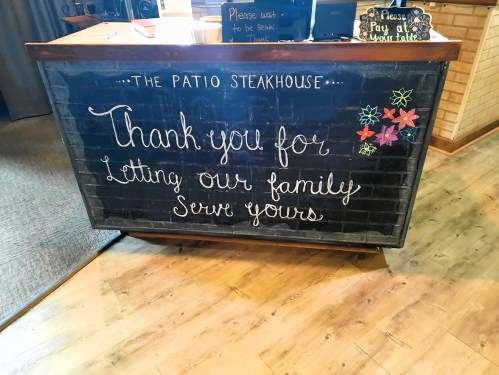 Chalkboard sign at a restaurant thanking customers for their support, decorated with colorful flowers.