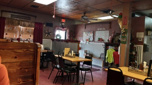 Cozy diner interior with wooden tables, black chairs, and festive decorations. A chalkboard displays the daily specials.
