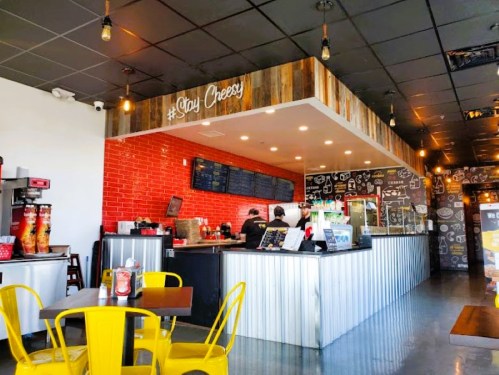 A cozy restaurant interior with a red brick wall, wooden accents, and yellow chairs, featuring a counter and menu board.