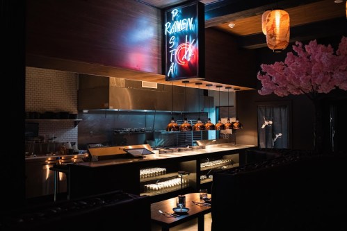 A modern restaurant interior featuring a neon sign, stylish lighting, and cherry blossom decor.