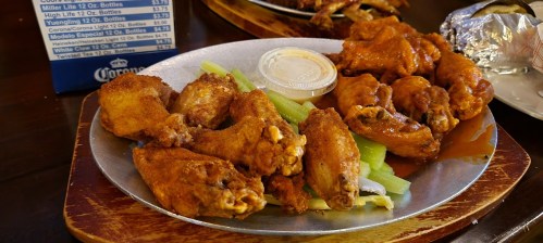 A plate of crispy chicken wings with celery sticks and a side of dipping sauce.