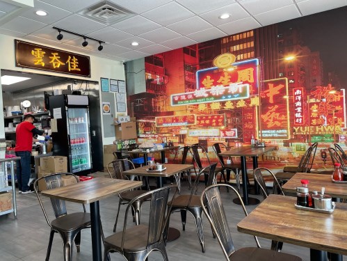 A cozy restaurant interior with wooden tables, metal chairs, and a vibrant neon city mural on the wall.