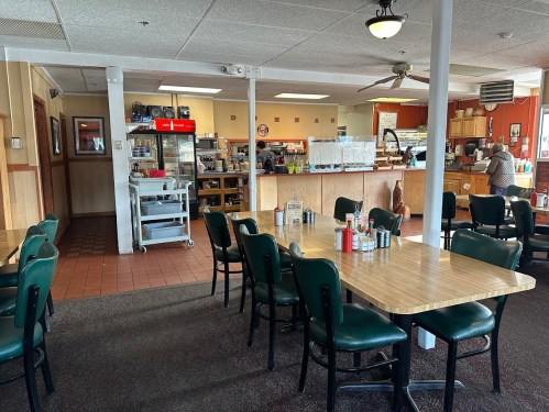 A cozy diner interior with empty tables, a counter, and a kitchen area in the background.